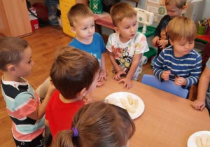 Dzieci stoją przy stoliku i próbują jabłek, śliwek i gruszek